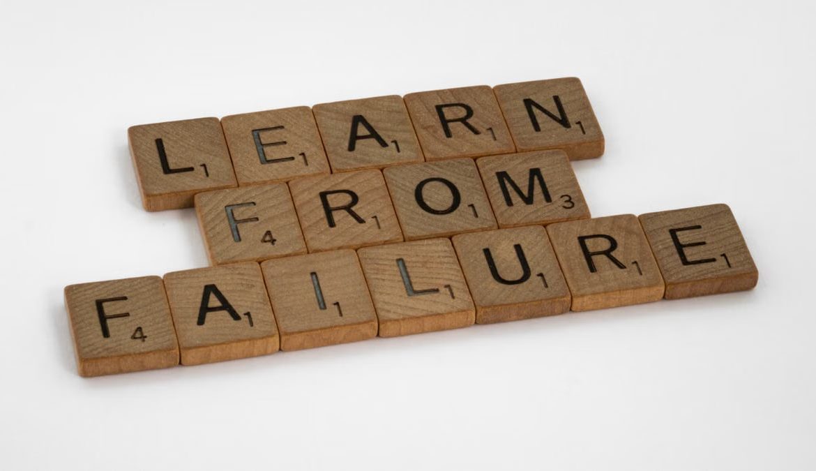 Wooden Scrabble tiles spelling 'Learn from Failure' on a white background, promoting resilience.